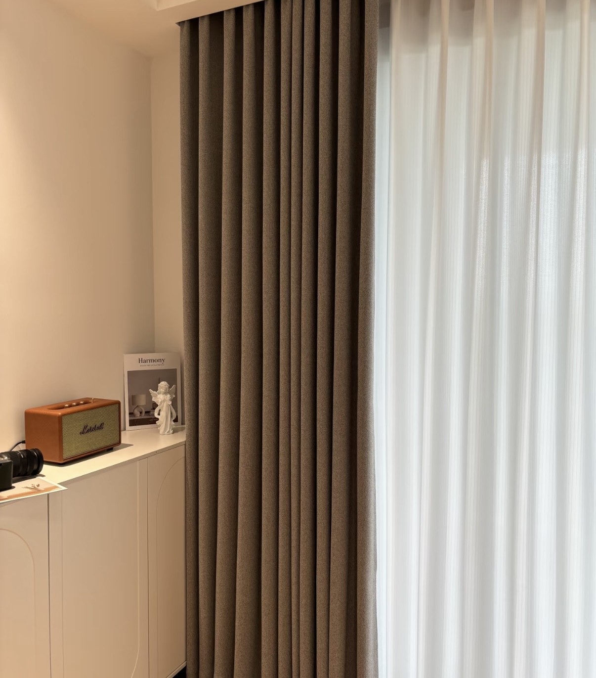 Brown and white curtains hanging in a room with a white cabinet and a small figurine.