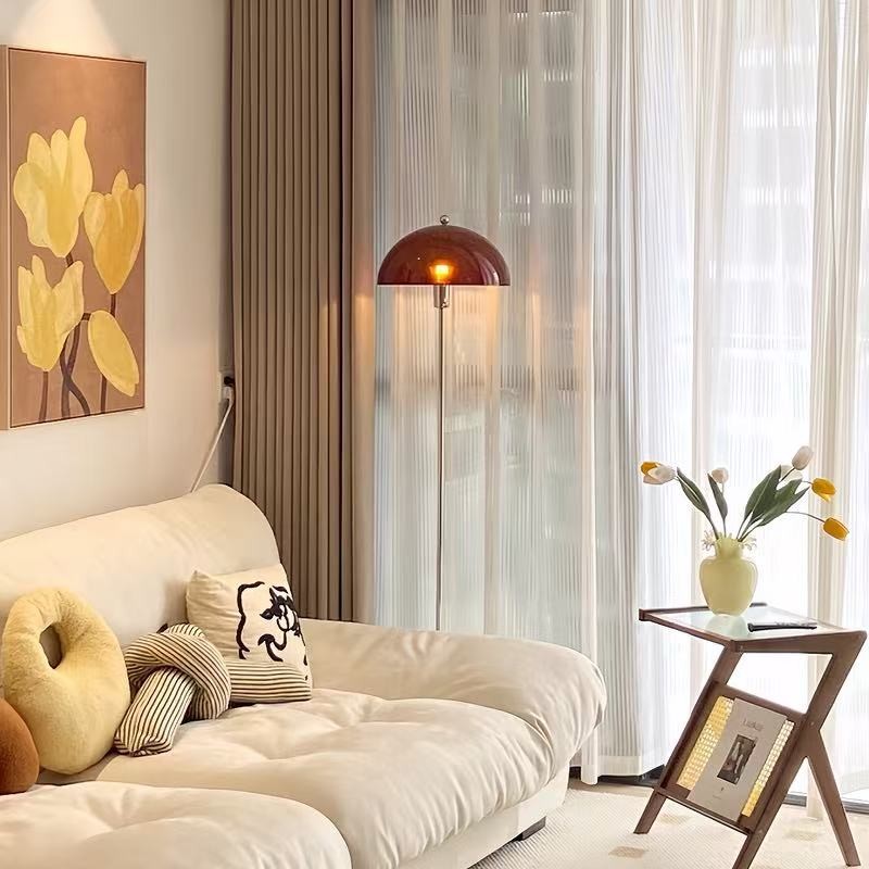 A cozy living room corner featuring a cream-colored sofa, decorative pillows, a floor lamp, sheer curtains and tulips.